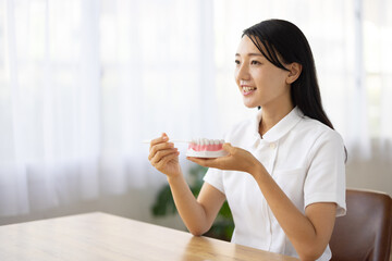 Woman in white coat demonstrating tooth brushing with dental model