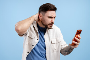 Young man reading puzzling message on mobile phone, showing doubt and feeling worried