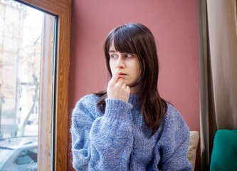 Thoughtful woman by the window in a cozy sweater