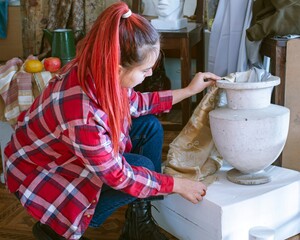 Young woman working in art studio. Artist arranging objects for still life in her studio.