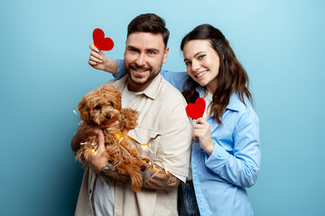 Happy couple holding red hearts and a cute puppy celebrating Valentine's Day