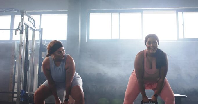 Diverse female duo in gymwear swinging kettlebells from chest hinging squats in gym training