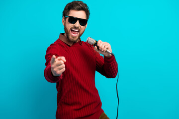 Young man sings into microphone wearing red sweater against blue background