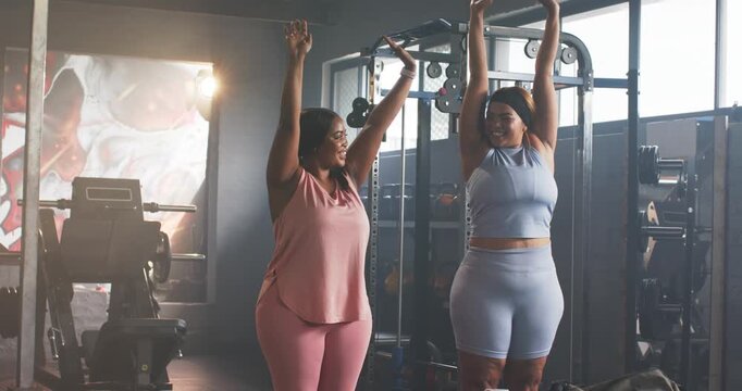 Instructor guiding African American trainee overhead and forward folding at gym with cable machine