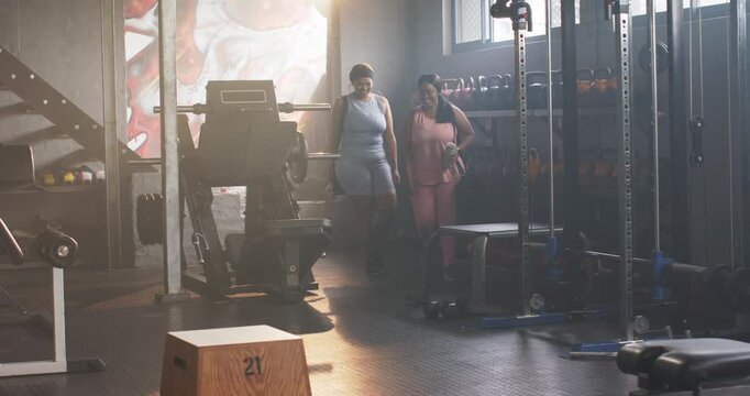 Mid-age women entering gym through doorway, walking past plyo 21 with duffel and shaker prepping
