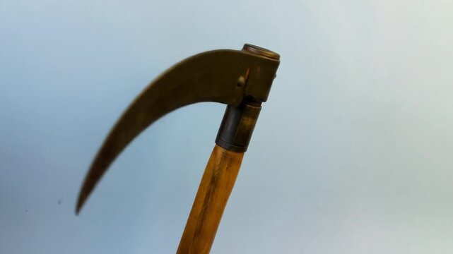 A close-up shot of a curved blade tool with a wooden handle against a plain blue-gray background