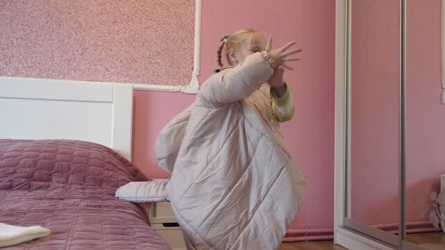 little girl putting on a large quilted jacket near the mirror, little girl tries on a beige down jacket in the bedroom, Child in an oversized down jacket