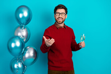 Young man with glasses celebrates with balloons and champagne against blue background
