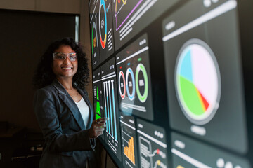 A professional Indian businesswoman interacts with a large digital dashboard displaying charts and analytics in a modern office. Leadership, planning, and data-driven strategy in tech-driven business.