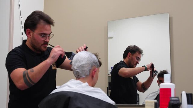 Barbershop mirror focus on hairdresser bleaching customer&rsquo;s head to change hair color