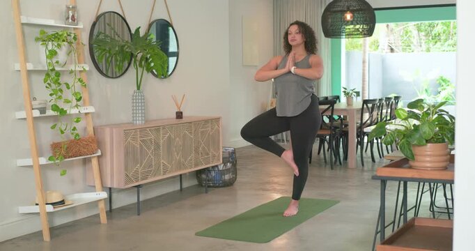 Adult African American woman following cue, moving tree into forward fold at home on green mat