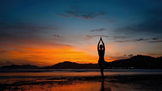 Silhouette of a person in the tree yoga pose on a beach at sunset with an orange sky.