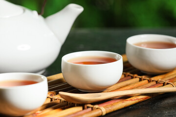 Bamboo mat with teapot, cups of tea and spoon for ceremony on black grunge table outdoors, closeup