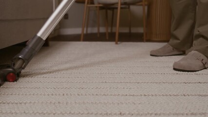 Low section of unrecognizable person cleaning carpet with vacuum in cozy living space
