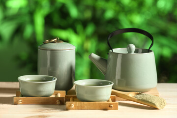 Teapot with cups of matcha tea and spoon for ceremony on wooden table outdoors, closeup