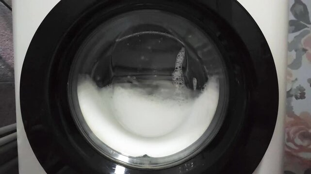 white soapy detergent foam spinning inside washing machine, slow motion closeup view