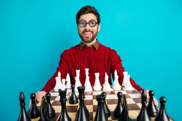 Happy man with chessboard and oversized glasses posing against blue background in red sweater
