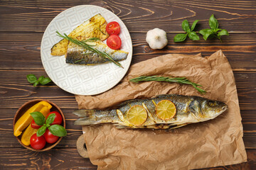 Delicious cooked seabass fish with tomatoes, herbs, garlic and bell pepper slices on wooden background