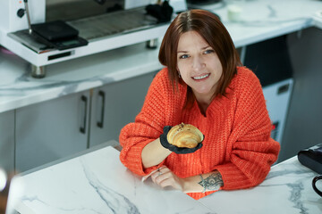 Young woman offering croissant in gloved hand at cafe workstation