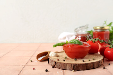 Bowl of tasty ketchup, fresh tomatoes and basil leaves on beige tile table against white wall