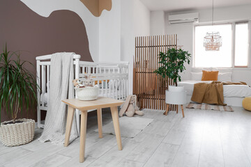 Interior of stylish room with big bed, baby crib and folding screen