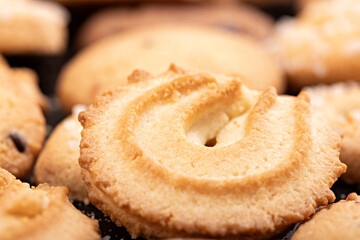 Close-up of a classic Danish butter cookie highlighting its golden color, crumbly texture, and decorative swirl shape. The shallow depth of field emphasizes the surface details and buttery crisp edges