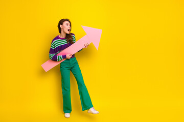 Young woman in striped sweater holds pink arrow against yellow background creating bold fashion and...