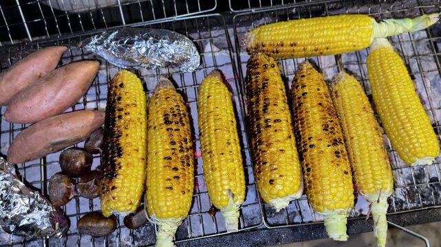 Close up 4K shot of corn sweet potatoes and chestnuts roasting on a charcoal grill showing detailed texture warm tones and a rustic outdoor cooking atmosphere.
