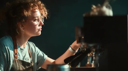 Barista with curly hair and glasses wearing an apron, preparing coffee at a vintage espresso machine.