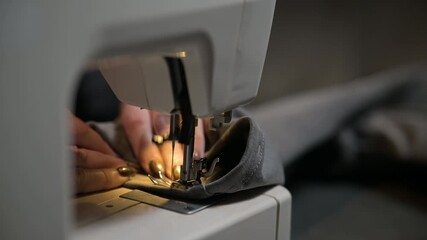 Close up side top view of cropped female hands sewing white fabric on professional manufacturing machine at seamstress workplace. Tailor hands holding textile for dress production. Blurred background