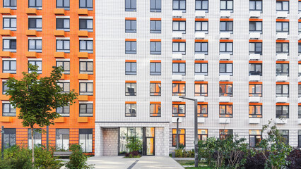 Modern residential apartment building with orange white tiled facade, large square windows, green landscaped courtyard  trees, contemporary urban architecture concept for real estate  city development
