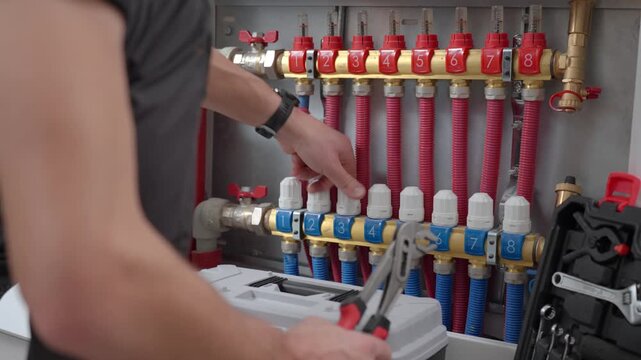 Close-up of technician adjusting control knobs on underfloor heating manifold with with red and blue pipes in circuits. Concept of heating system maintenance and plumbing service
