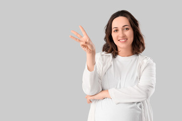 Young pregnant woman showing three fingers on light background. Rules concept