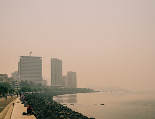 Mumbai, India Coastal urban view of Marine Drive in Mumbai with people sitting along the seawall and high-rise buildings fading into warm haze. A calm waterfront cityscape at the Arabian Sea.