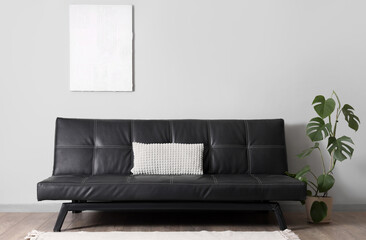 Stylish modern black sofa with pillow and houseplant near grey wall