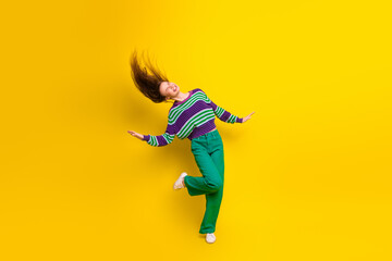 Young woman dancing joyfully in striped sweater and green pants against bright yellow background