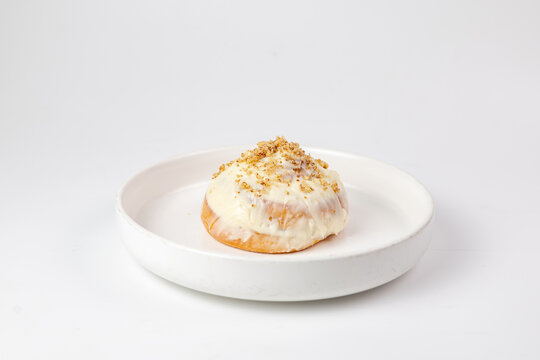 Cinnabon roll with cream cheese glaze and crumb topping on white plate against clean background