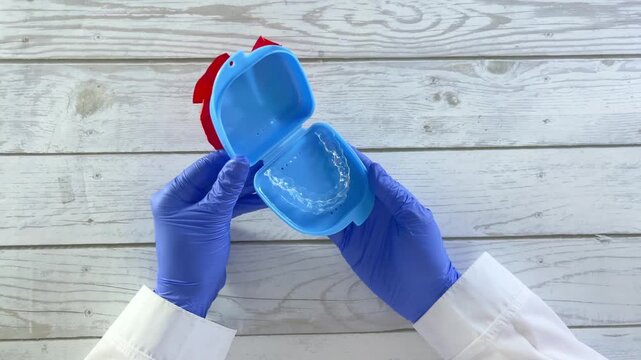 Blue dental retainer case adorned with a red bow, held by gloved hands against a wooden background