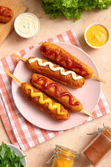 Plate of tasty corn dogs with different sauces on beige background