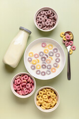 Bowls of colorful sweet cereal rings with milk on green background