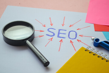 Magnifying glass on paper. SEO or Search Engine Optimization concept. Paper with magnifying glass, binder note and pen with arrow pointing at SEO letter abbreviation on paper.