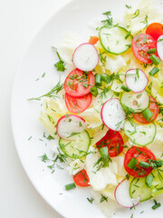 Plate with fresh spring salad veggies and iceberg salad covered in olive oil, top view of plate with vitamin meal.