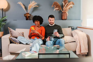 Joyful couple engaged in their own worlds while using their smartphones, sharing moments together in a cozy living space. Each is immersed in their mobile devices, fostering connection and