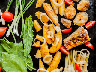 Oven pan with sliced baked potatoes, fish steaks and vegetables with onion on table.