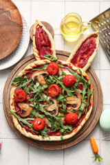 Wooden board with tasty pizza for Easter celebration on white tile background