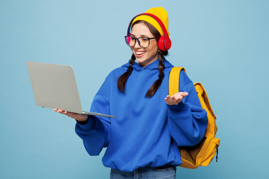 Young happy smart IT woman student wear casual clothes yellow backpack bag headphones hold books use work on laptop pc computer isolated on plain blue color background. High college lifestyle concept. - Powered by Adobe