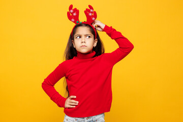 Merry little girl wear red clothes fun decorative deer horns on head posing put hand on head scratch temples isolated on plain yellow background. Happy New Year Christmas celebration holiday concept.