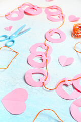 Garland made of pink paper flags with hearts and scissors on blue background. Valentine's Day celebration
