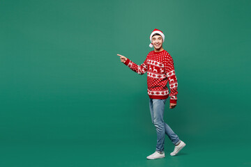 Full body side view merry young man he wear red warm cozy Christmas sweater Santa Claus hat posing...