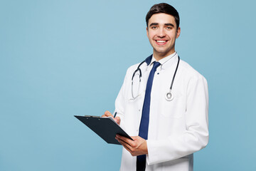 Young male doctor man wears white medical gown suit work in hospital clinic office hold clipboard sign paper documents isolated on plain blue background studio portrait. Healthcare medicine concept.